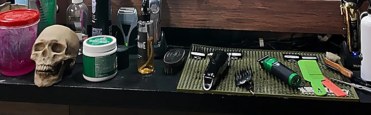 Mesa de trabajo con máquinas de corte sobre un tapete verde, peines, productos y un cráneo decorativo